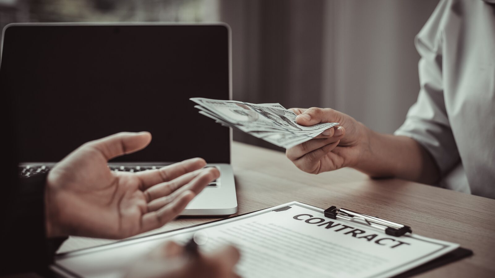 Cash being passed across a desk over a contract