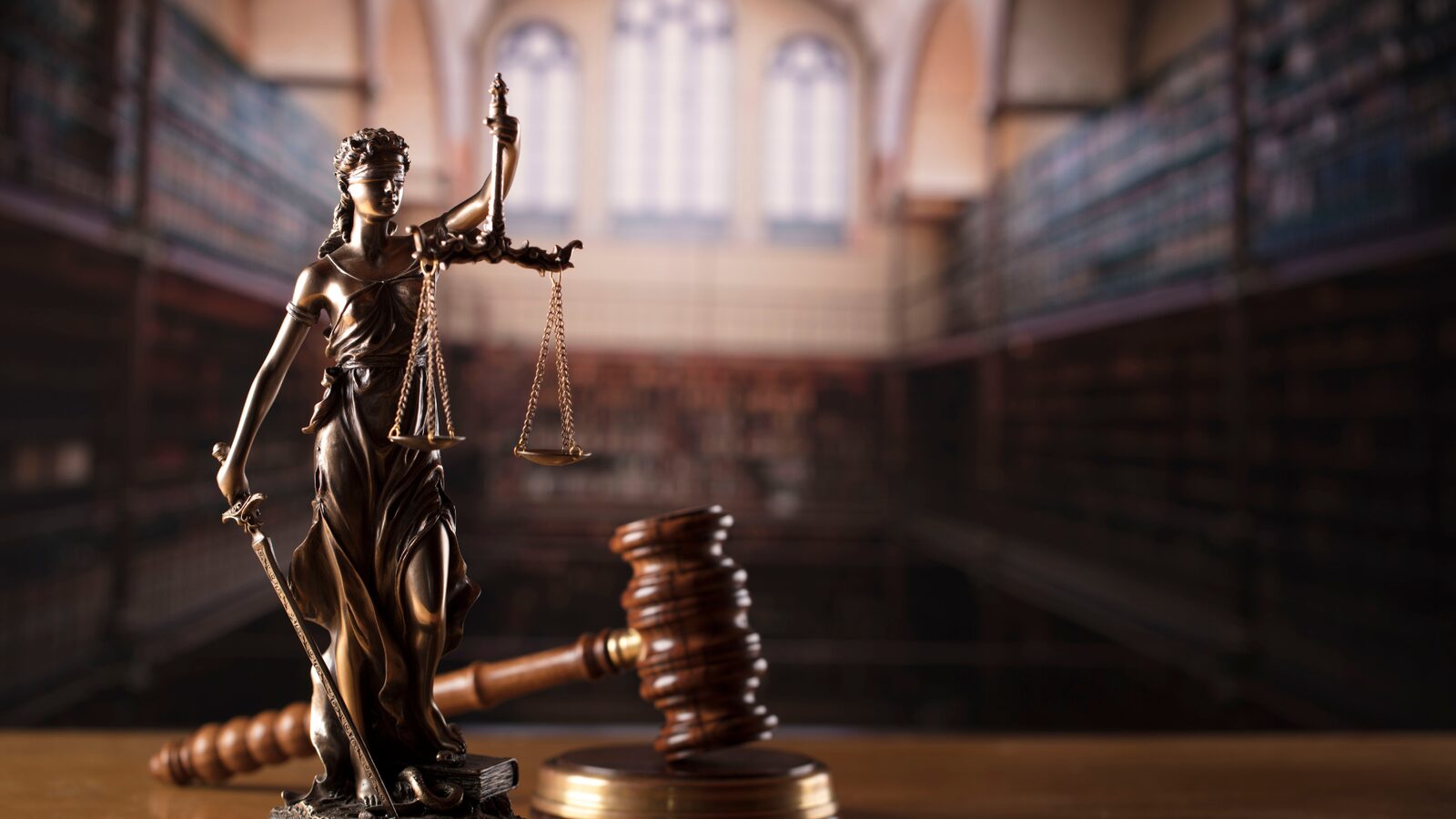 A statue of Lady Justice beside a gavel in a law library